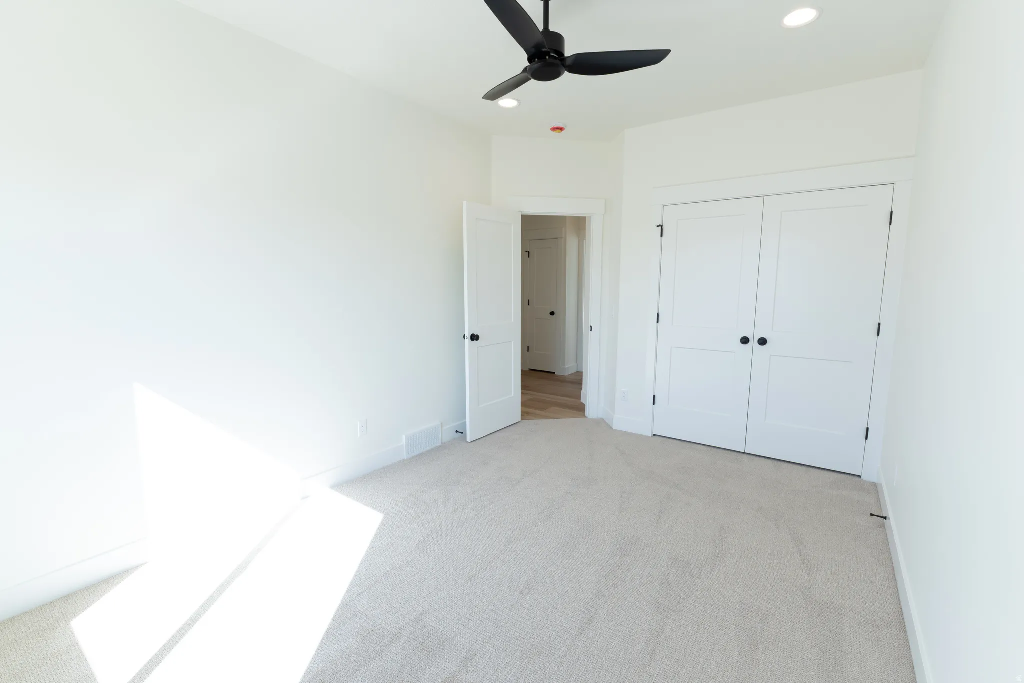 Neutral tone carpeting, recessed ceiling lighting, a black ceiling fan, white paneled doors, and white trim