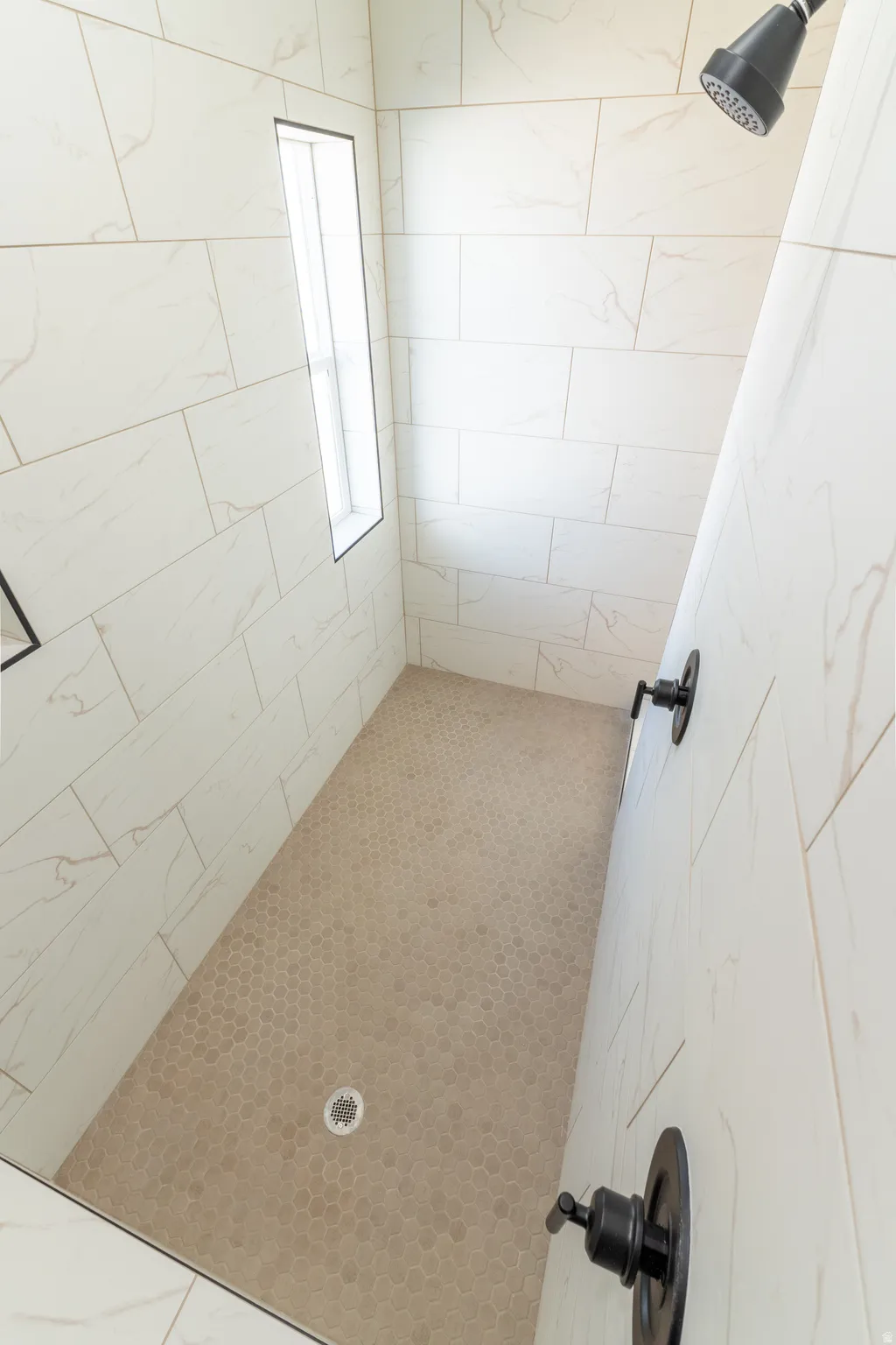 Spacious shower with large format wall tile, hexagonal floor tile, matte black fixtures, and an integrated window. Master shower. Walk-in
