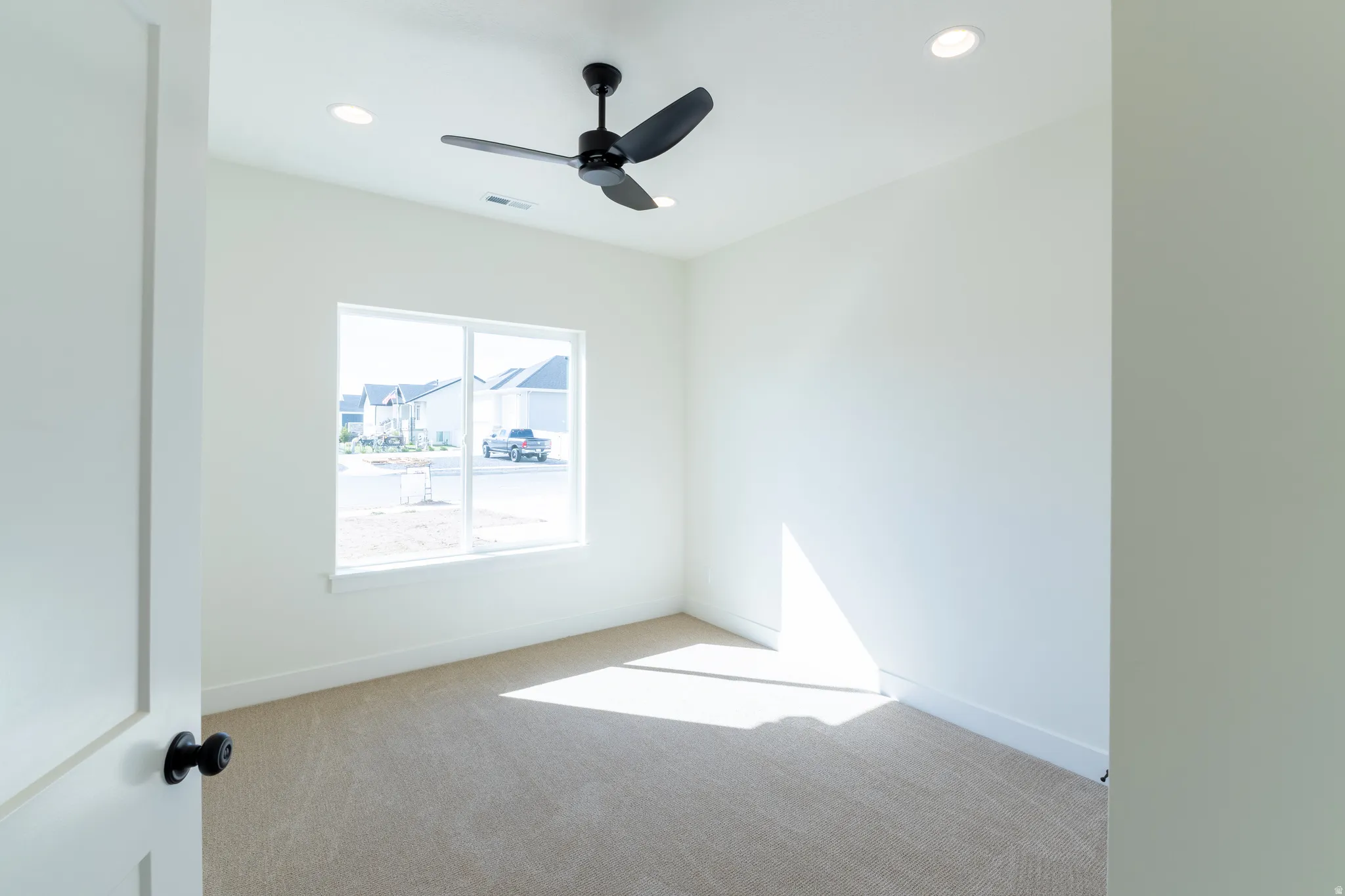 Recessed lighting, ceiling fan, expansive window, neutral wall paint, and plush carpet