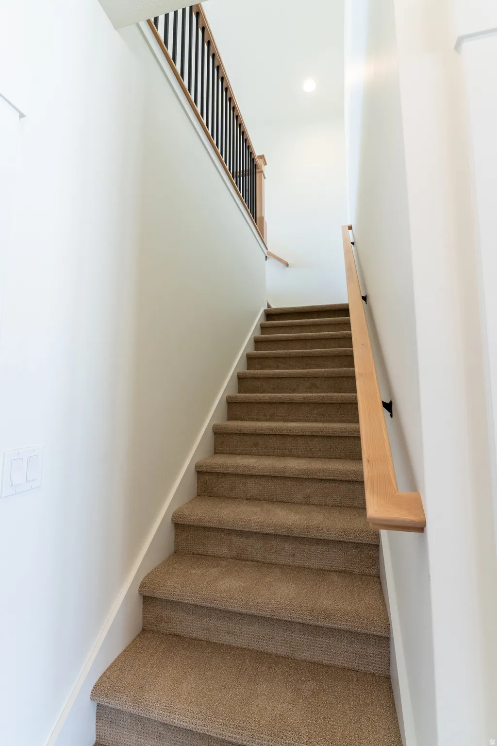 Carpeted staircase with light wood railings and wrought iron spindles