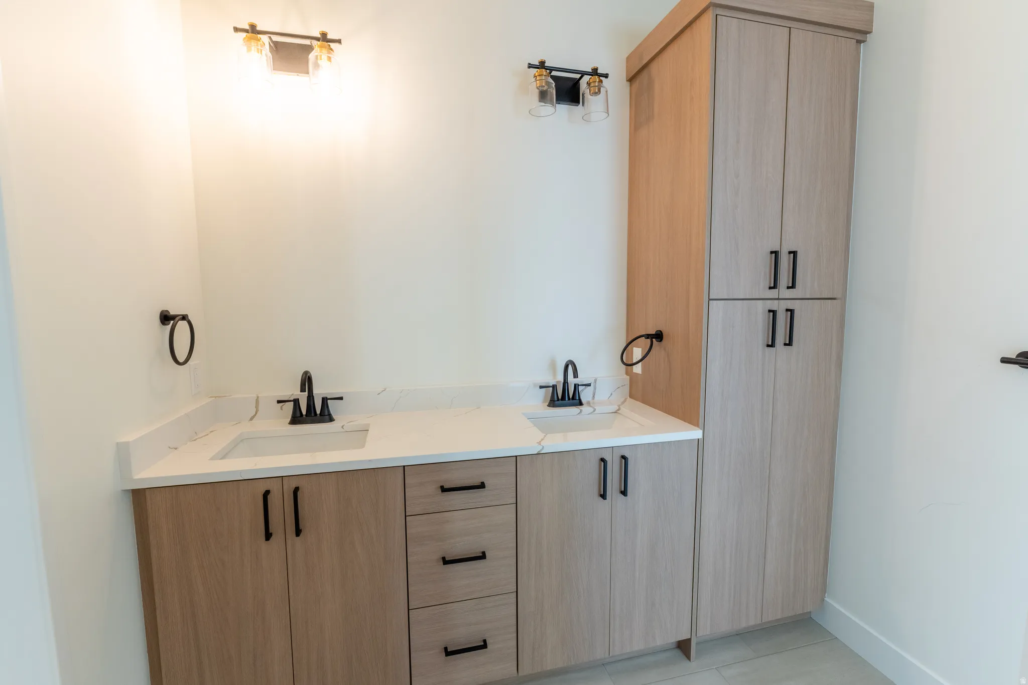 Dual vanity with integrated sinks, light wood-finish cabinetry, white countertop, and black fixtures