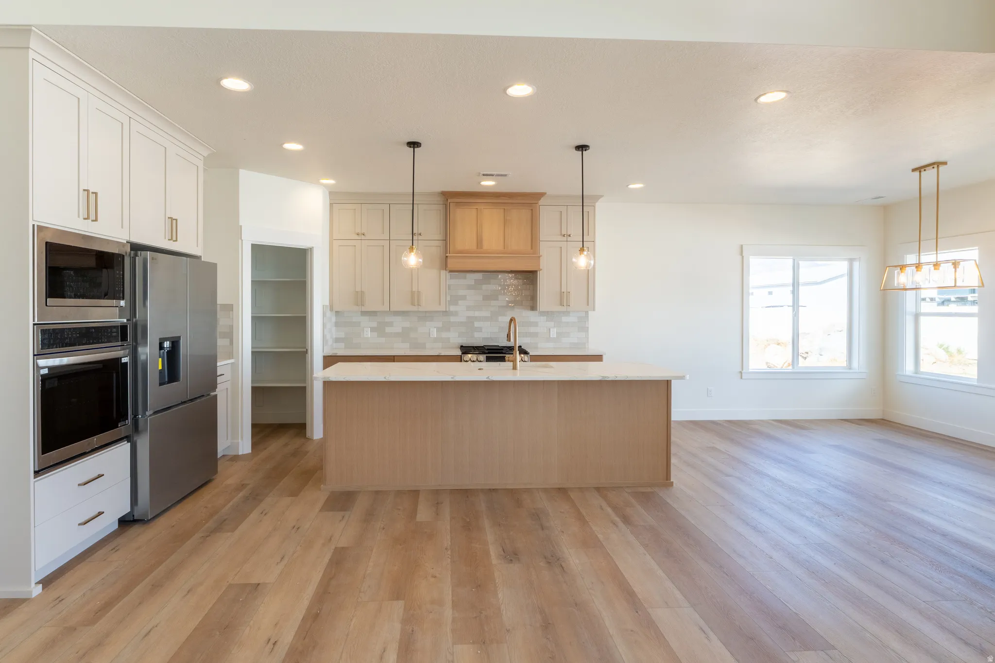 Open-concept kitchen featuring stainless steel appliances, a center island with a stone-finish countertop, wood-finish flooring, and recessed lighting