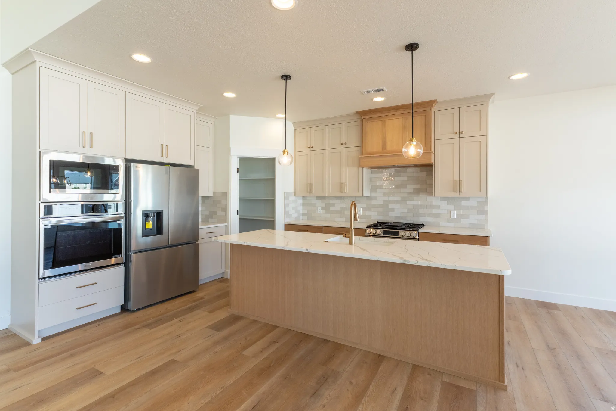 Modern kitchen featuring an expansive center island with a stone countertop, stainless steel appliances, wood-finish flooring, and light-toned cabinetry