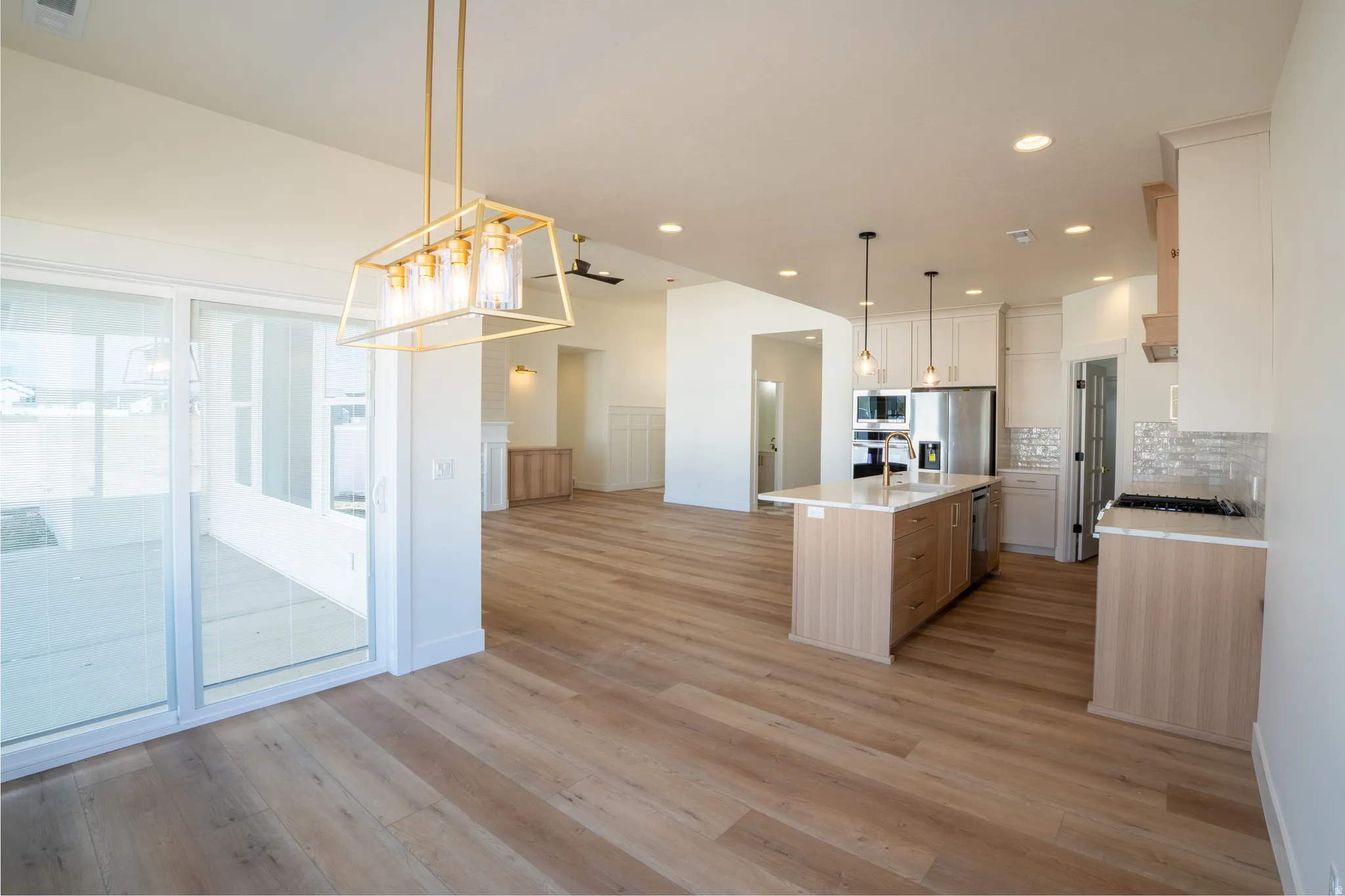 Open-concept living space featuring wood-finish flooring, a kitchen island with pendant lighting, stainless steel appliances, a tiled backsplash, and sliding glass patio doors
