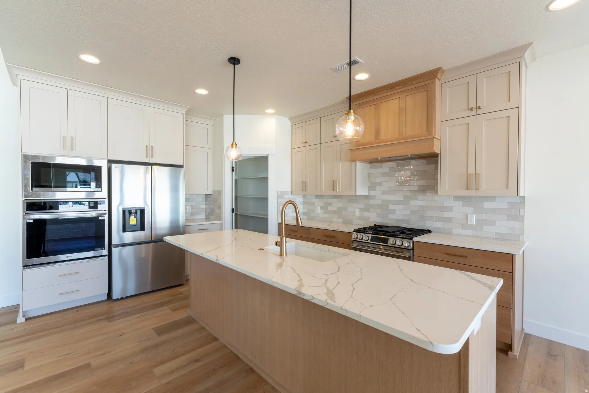 Spacious kitchen featuring an expansive island with a white countertop, built-in stainless steel appliances, two-tone cabinetry, and wood-finish flooring