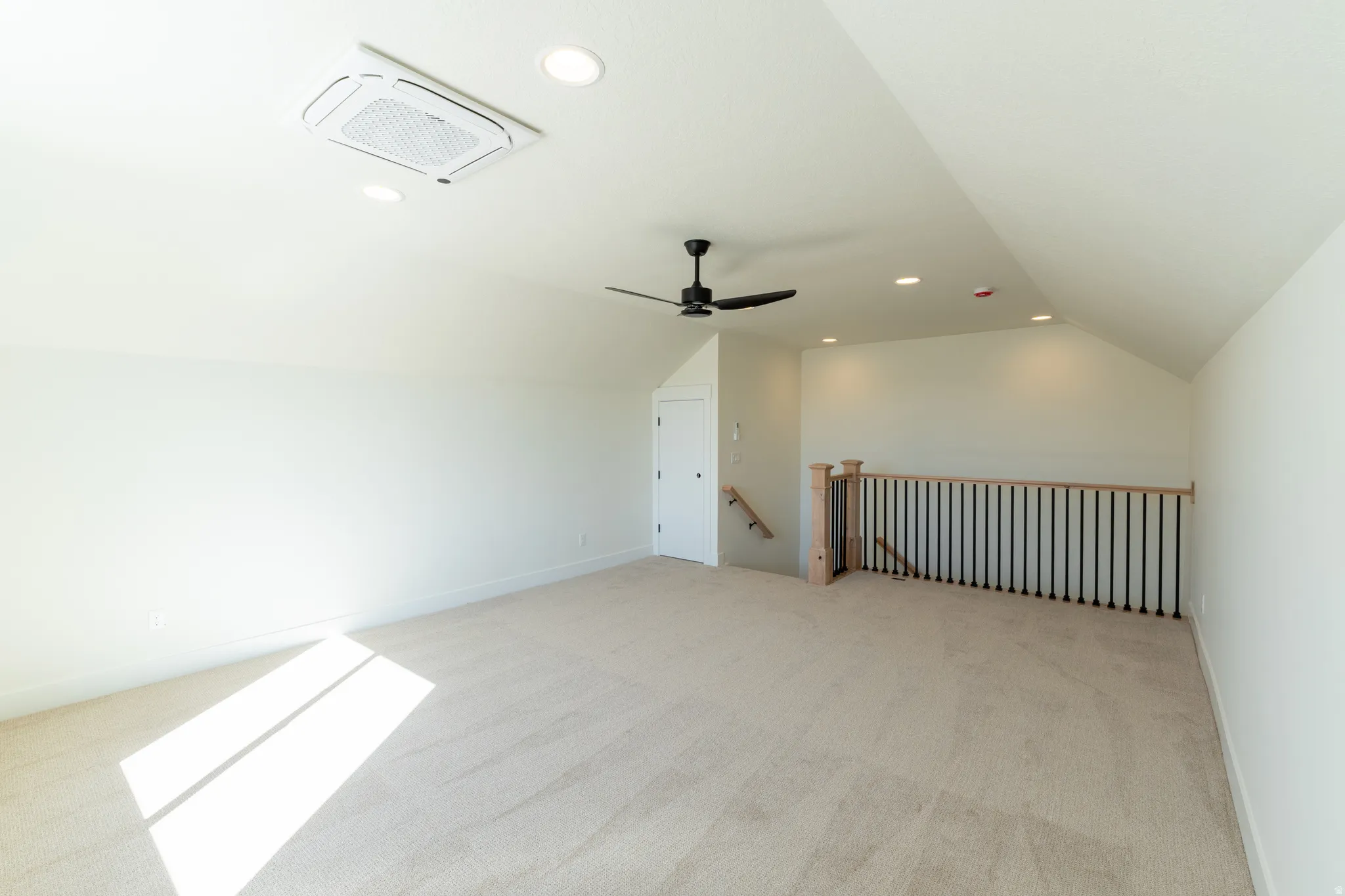 Spacious carpeted room featuring a sloped ceiling, recessed lighting, a ceiling fan, and a contemporary railing with black balusters. Loft upstairs.