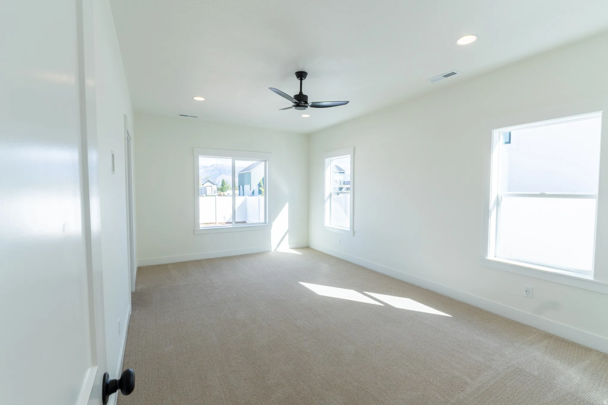 Neutral-toned carpeting, white walls, multiple windows, a ceiling fan, and recessed lighting
