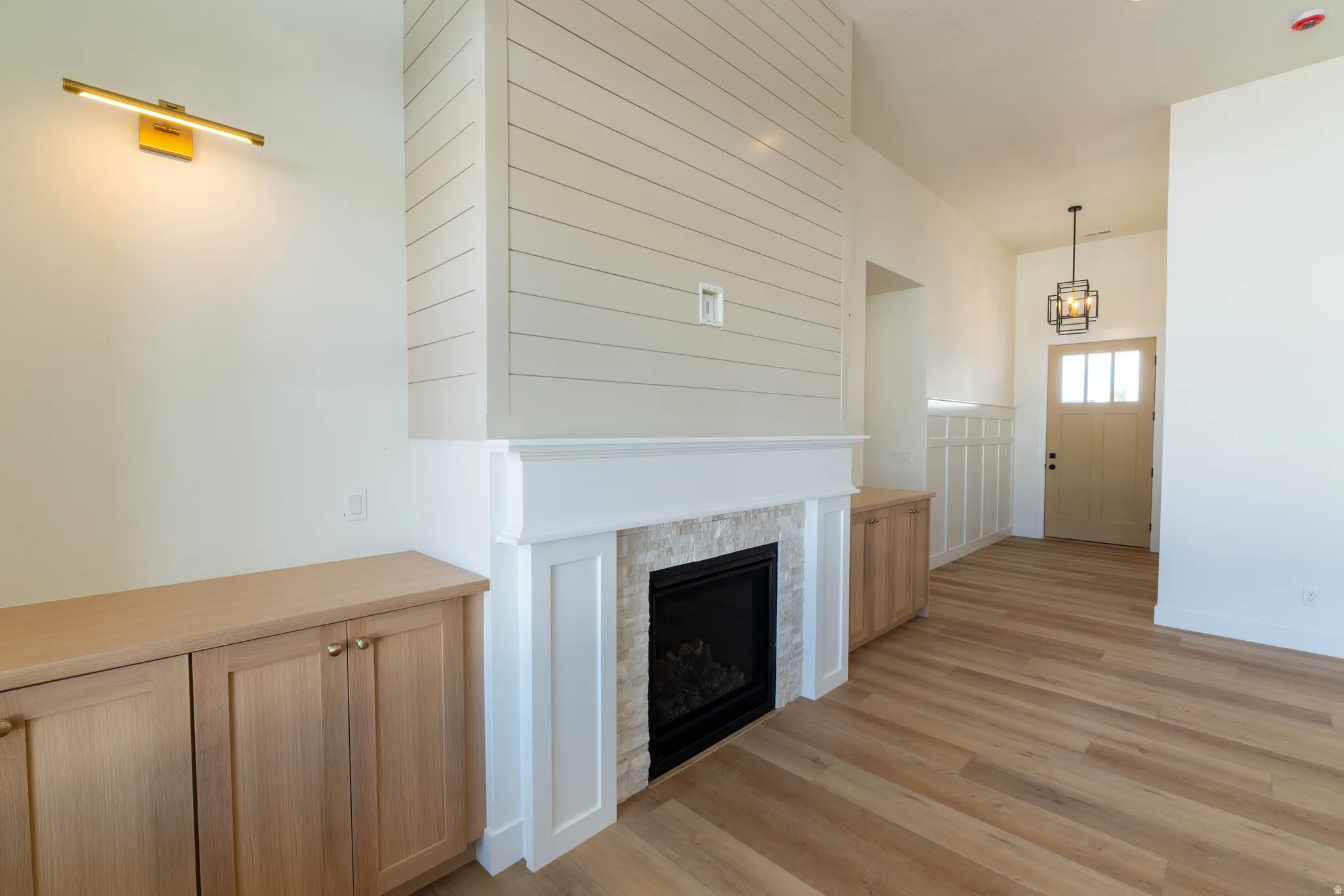 Built-in fireplace with stone surround, shiplap accent wall, wood-finish flooring, built-in cabinetry, and a solid wood entry door