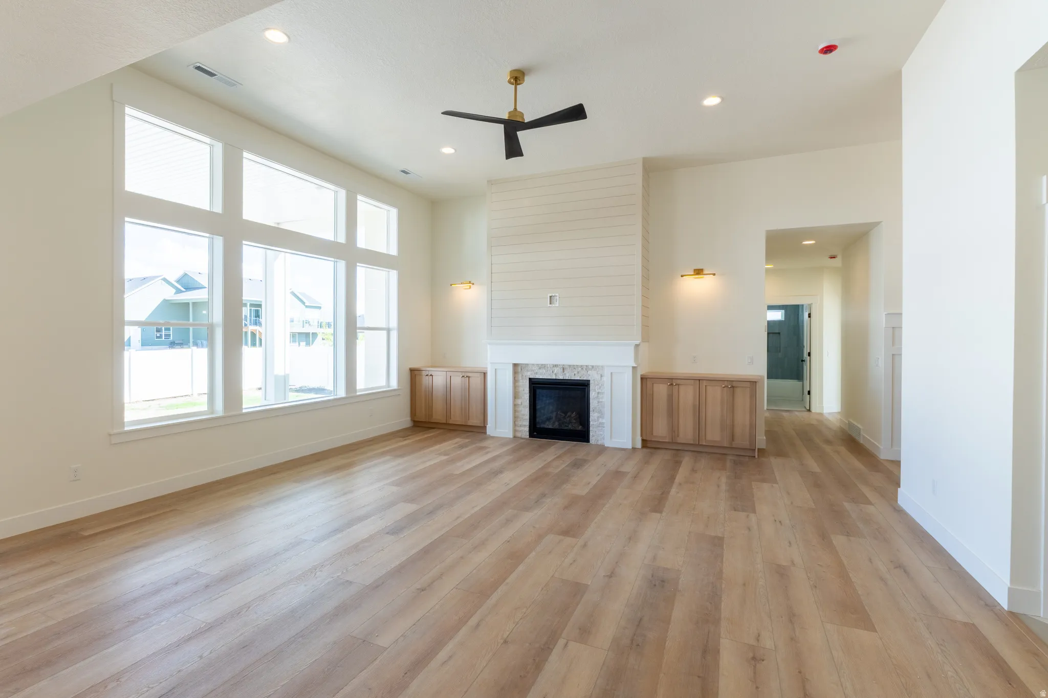 Spacious living area featuring wood-finish flooring, a contemporary fireplace with white mantel, built-in cabinetry, and large windows