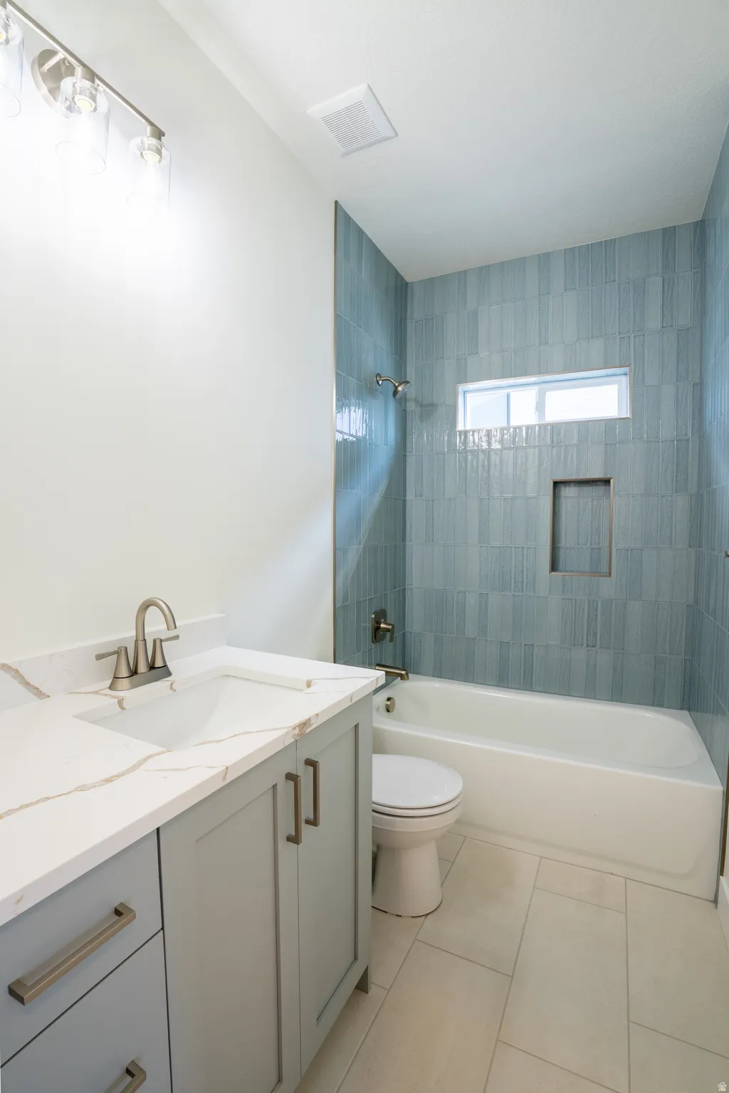 Built-in bathtub with shower featuring blue tiled surround and recessed shelf