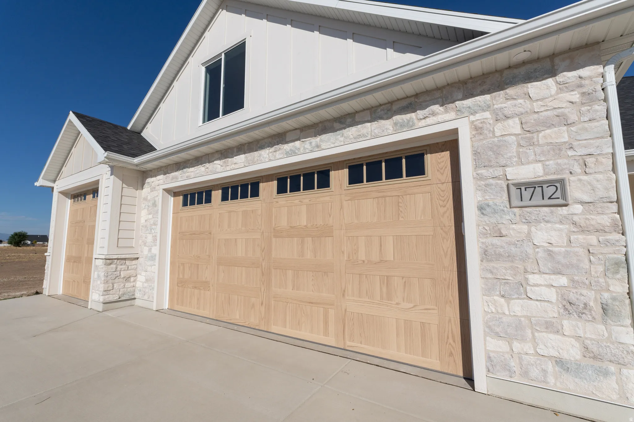 Stone veneer exterior with light wood-finish garage doors featuring upper window panels, and a concrete driveway