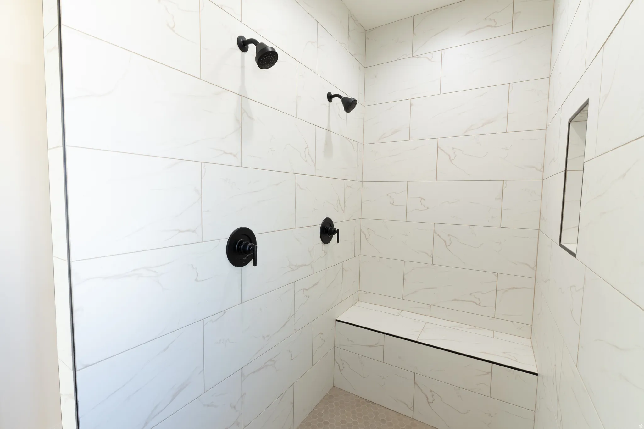 Shower enclosure featuring white tile with subtle veining, matte black fixtures, a built-in shower bench, and a recessed shower niche