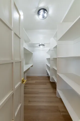 Walk-in pantry featuring extensive built-in shelving, wood-finish flooring, and recessed ceiling lighting