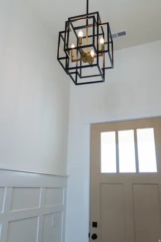 Modern geometric chandelier with brass accents, tall ceilings, board and batten wall paneling, and a light-colored entry door with glass inserts