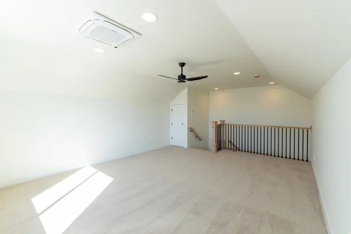 Spacious carpeted room featuring a sloped ceiling, recessed lighting, a ceiling fan, and a contemporary railing with black balusters. Loft upstairs.