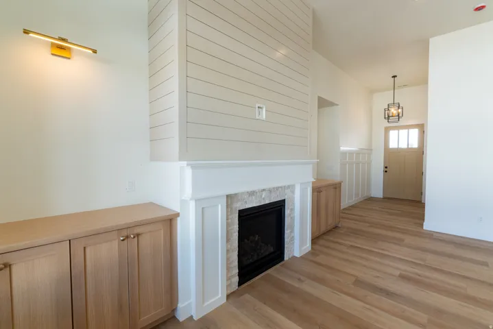 Built-in fireplace with stone surround, shiplap accent wall, wood-finish flooring, built-in cabinetry, and a solid wood entry door