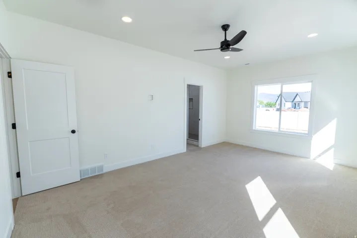 Recessed lighting, neutral carpeting, white interior doors with black hardware, modern ceiling fan, and large window. Master Bedroom
