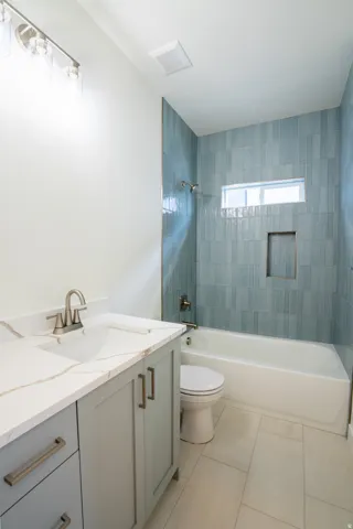 Built-in bathtub with shower featuring blue tiled surround and recessed shelf