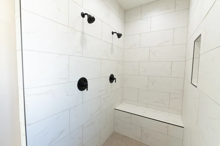 Shower enclosure featuring white tile with subtle veining, matte black fixtures, a built-in shower bench, and a recessed shower niche