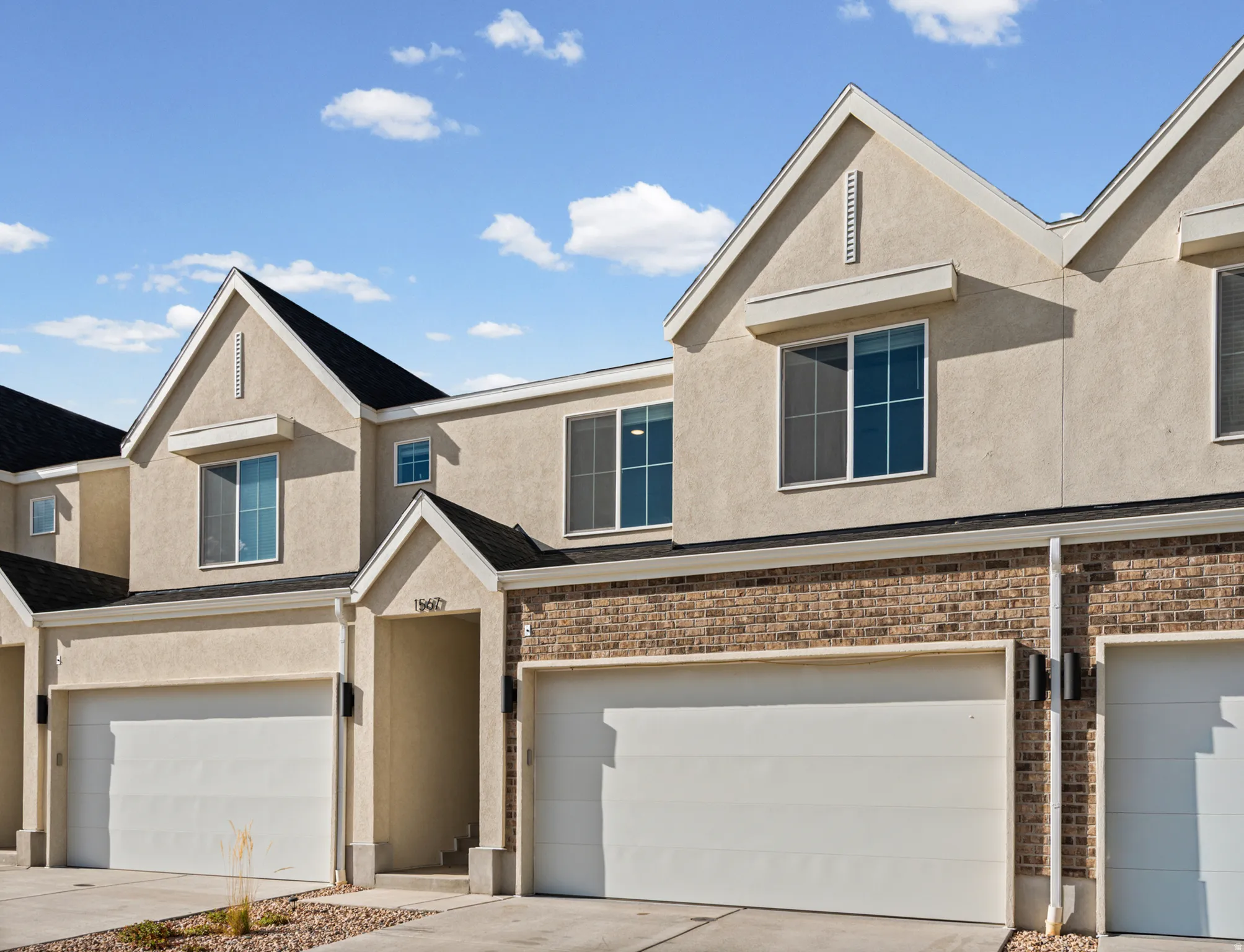 Contemporary exterior featuring stucco and brick accents, multiple gabled roofs, and two single-car garages