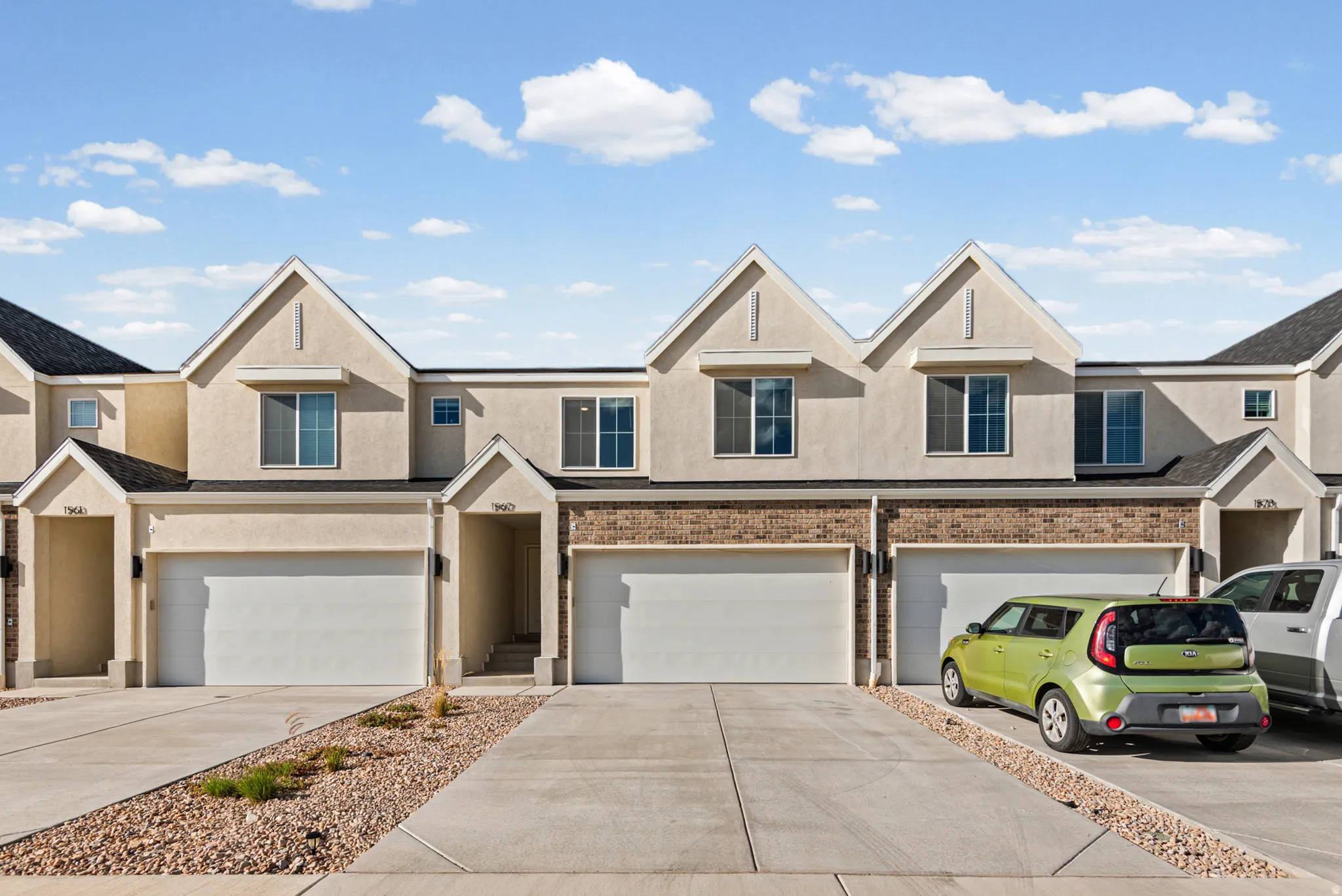 Stucco exterior with brick accents, attached garages, paved driveways, and peaked rooflines