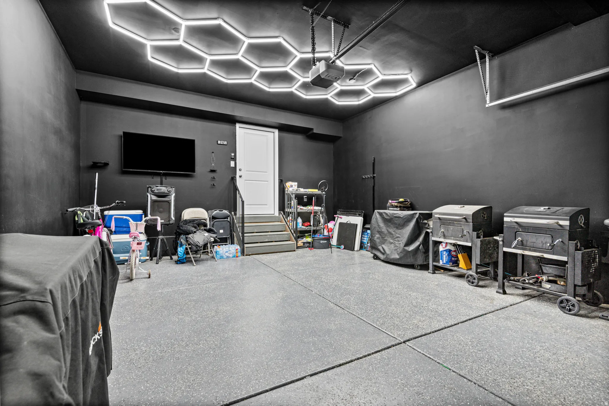 Oversized garage featuring a gray epoxy-coated floor, hexagonal ceiling light fixtures, a paneled door, and dark-painted walls