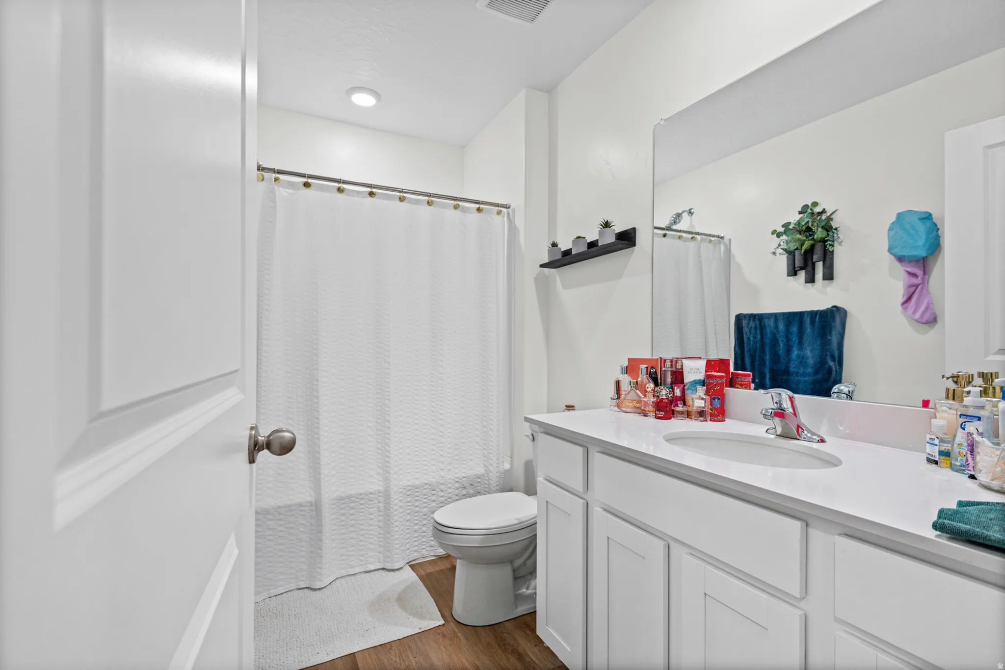 White vanity with a single basin sink, wall-mounted mirror, and wood-finish flooring