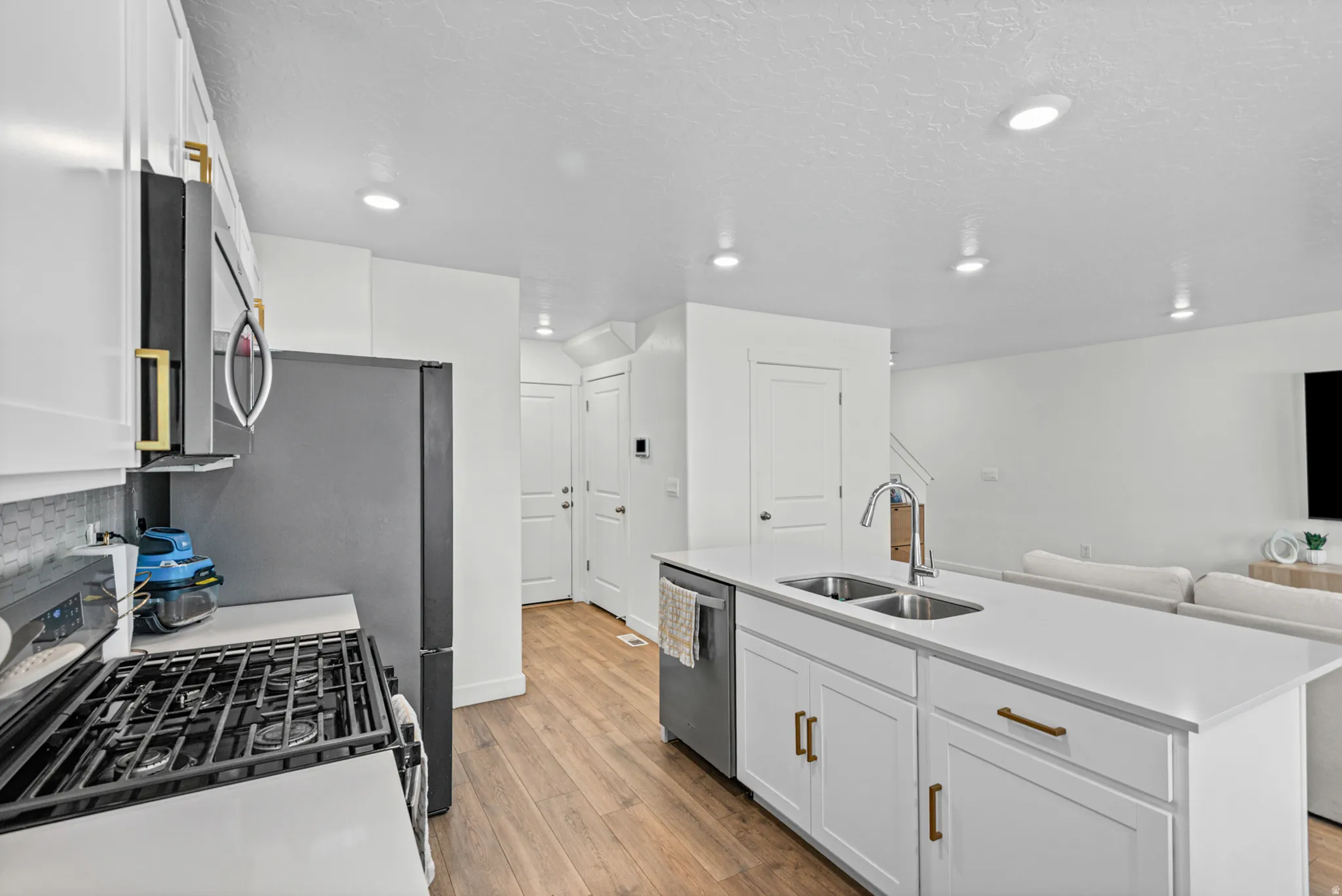 Spacious kitchen with white cabinetry, stainless steel appliances, a center island with a double sink, and wood-finish flooring