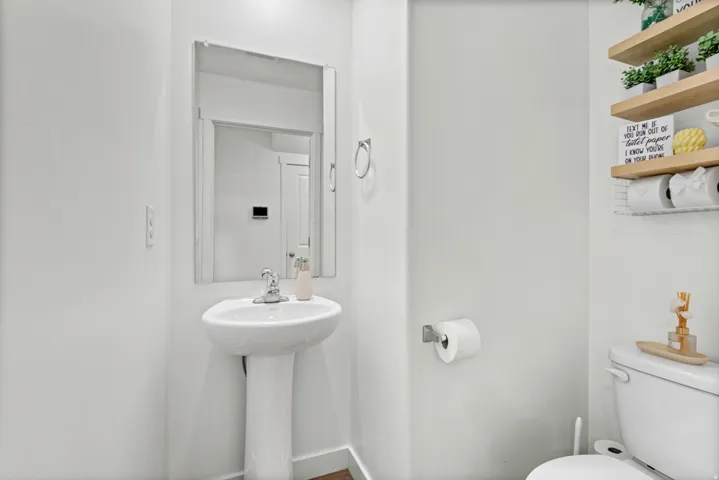 Pedestal sink with chrome faucet, wall-mounted mirror, and wood-finish floating shelves