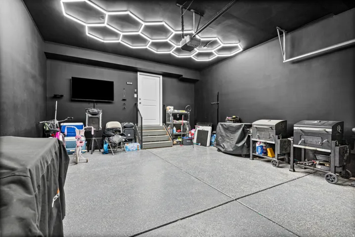 Oversized garage featuring a gray epoxy-coated floor, hexagonal ceiling light fixtures, a paneled door, and dark-painted walls