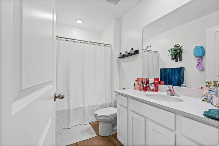 White vanity with a single basin sink, wall-mounted mirror, and wood-finish flooring