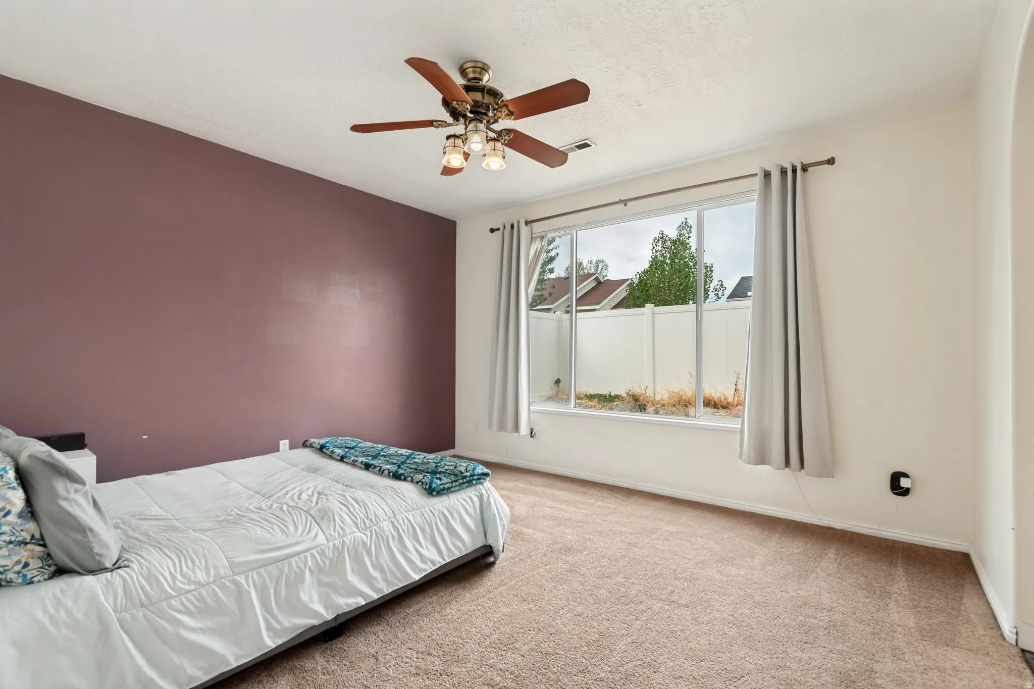 Expansive window with window treatments, ceiling fan with integrated lighting, and carpeted flooring