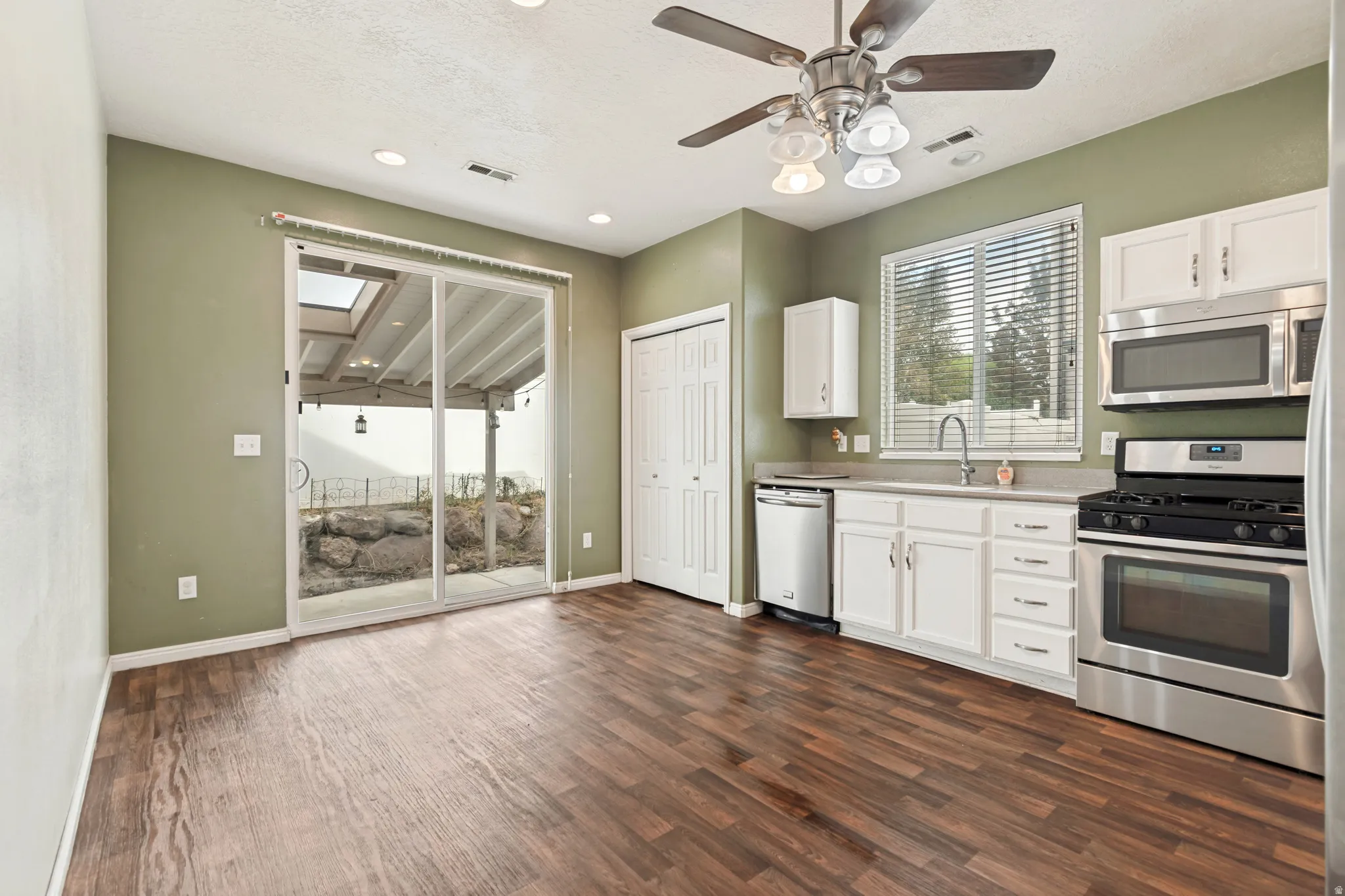 Kitchen featuring wood-finish flooring, white cabinetry, stainless steel appliances, and a ceiling fan