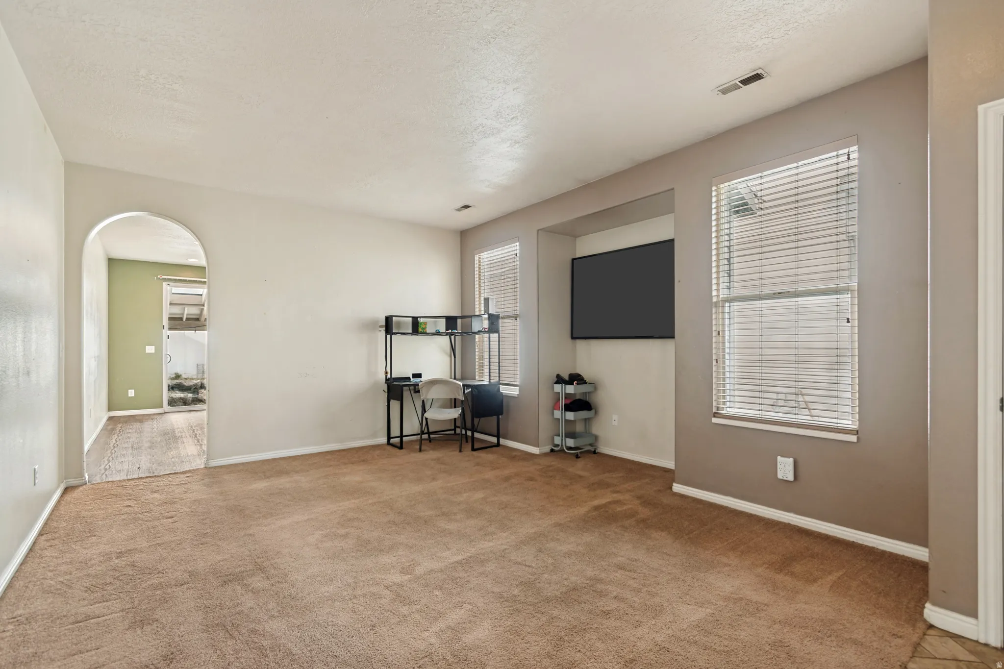 Arched doorway, built-in media niche, dual windows with blinds, and light-toned wall finishes