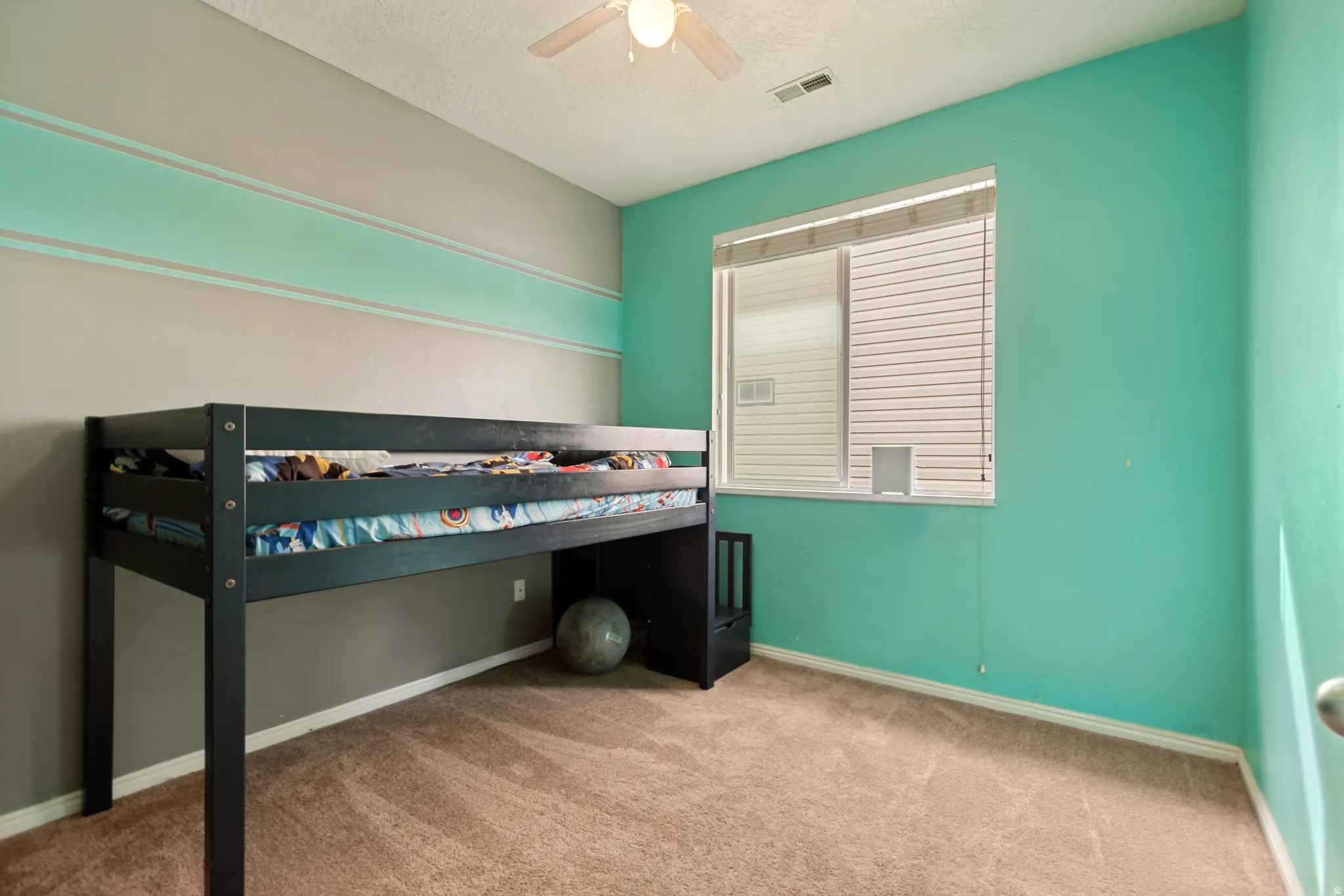 Carpeted flooring, a ceiling fan, and a window with blinds provide comfort and natural light