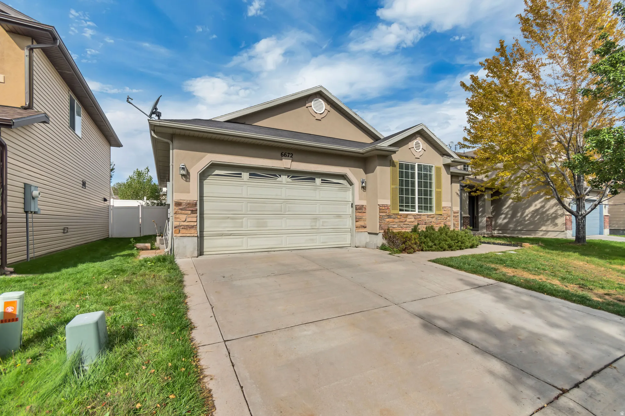Stucco exterior featuring a two-car garage, stone veneer accents, and a concrete driveway