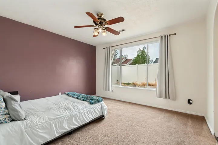 Expansive window with window treatments, ceiling fan with integrated lighting, and carpeted flooring
