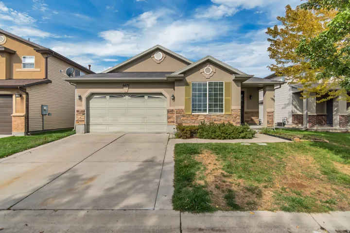 Stucco exterior with stone accents, attached garage, concrete driveway, and front landscaping