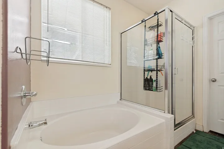Built-in soaking tub with chrome fixtures, glass-enclosed shower, and a privacy window