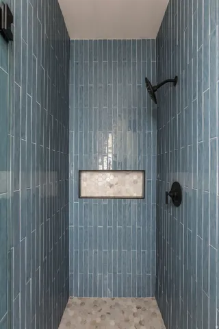 Vertical subway tile shower surround with integrated storage niche, pebble tile floor, and matte black fixtures