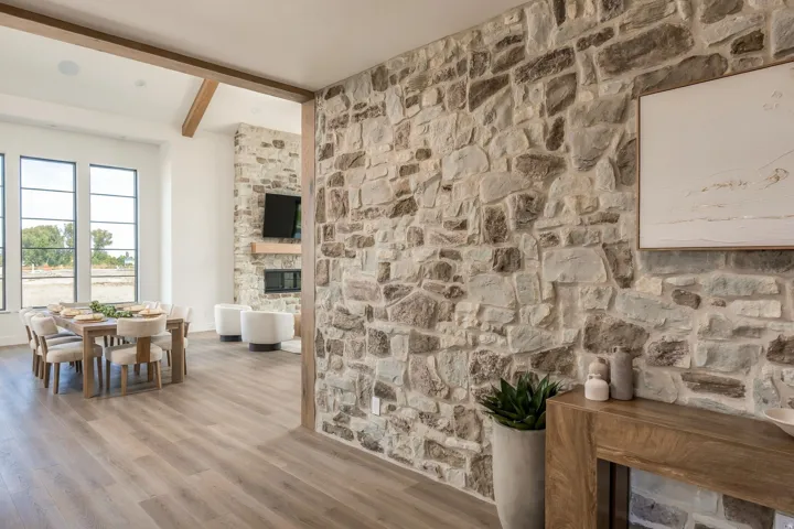 Stone accent wall, wood-finish flooring, wood ceiling beams, large multi-pane windows, and a stone-clad fireplace
