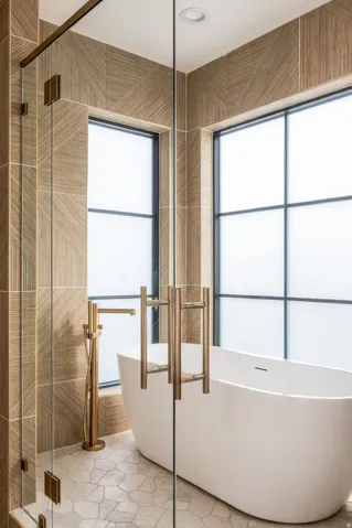 Freestanding soaking tub with a floor-mounted gold-toned faucet, glass-enclosed shower with gold-toned hardware, and mosaic tile flooring