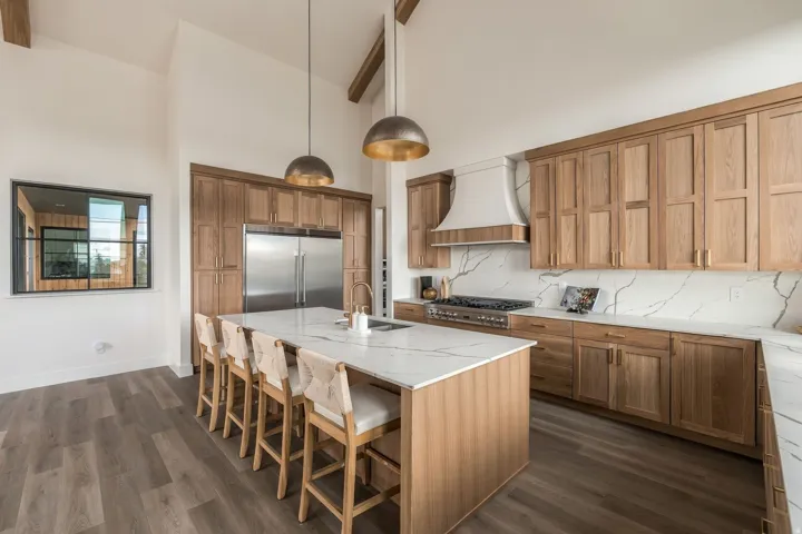 Vaulted ceiling with exposed wood beams, wood-finish flooring, custom wood cabinetry, stainless steel appliances, and a central island with a solid surface countertop