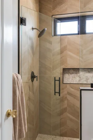 Glass-enclosed shower featuring chevron-patterned wall tile, a built-in mosaic tile niche, and a fixed window