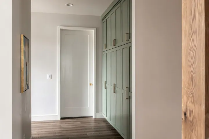 Hallway with wood-finish flooring, recessed lighting, white paneled door, and built-in cabinetry with brass hardware