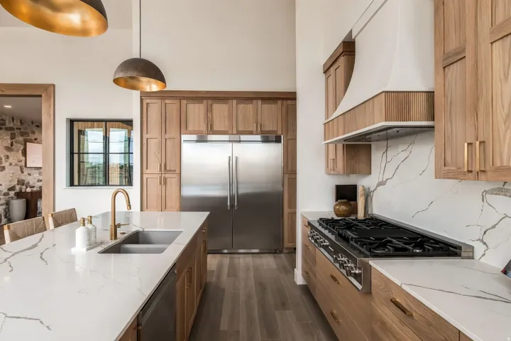 Gourmet kitchen featuring a stainless steel refrigerator, white countertops with veining, wood-finish cabinetry, and a gold-finish faucet