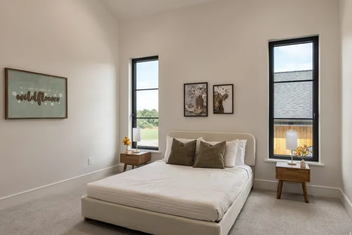 Vaulted ceiling, light neutral wall color, two tall windows with black frames, and light-colored carpeting