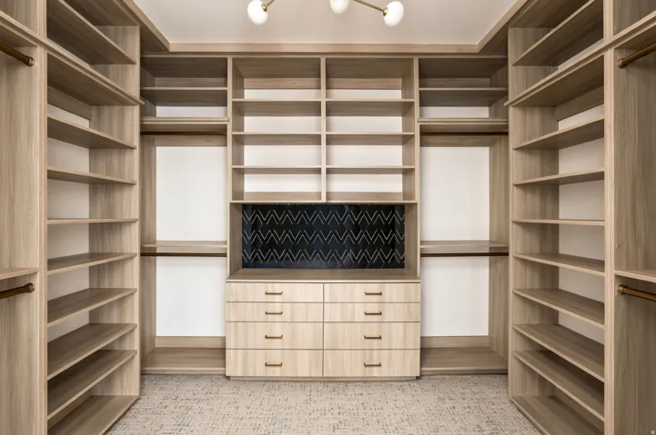 Custom closet system with light wood-finish shelving, integrated drawers, and brass hardware