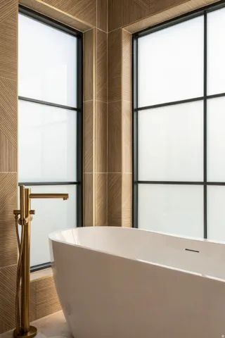 Freestanding soaking tub with a floor-mounted gold-tone faucet, complemented by large windows and patterned wall tile