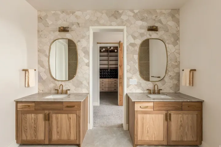 Dual wood-finish vanities with undermount sinks, stone countertops, and gold-tone fixtures